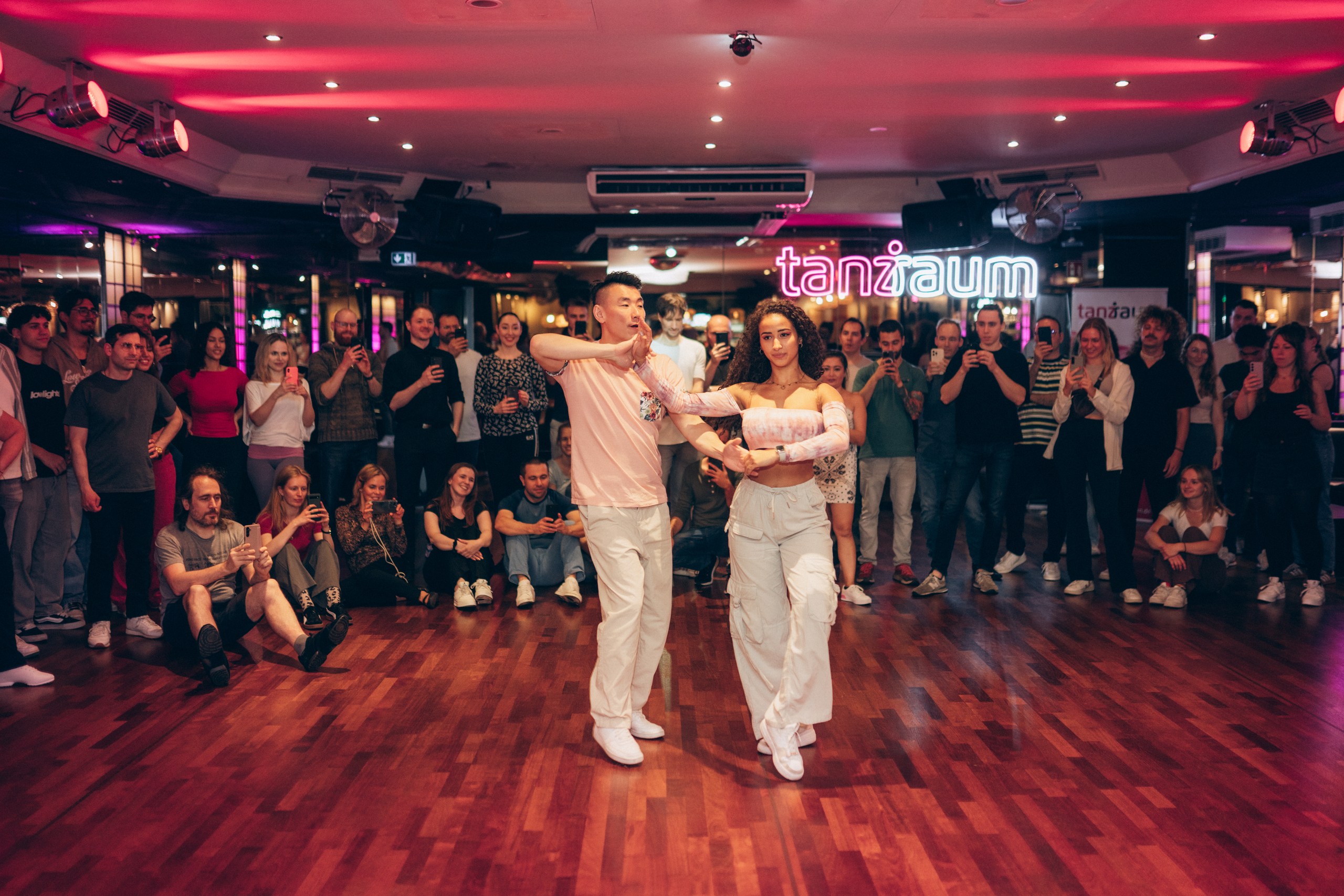 Zwei Bachata-Lehrer zeigen nach dem Bachata-Unterricht in einer Tanzschule in Köln eine Drehung, während die Schüler sie mit ihren Kameras aufnehmen
